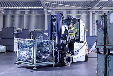 A Leadec employee driving with a forklift with a pallet of waste through factory. 